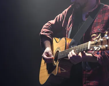 Male musician playing acoustic guitar in a dark room copy space.