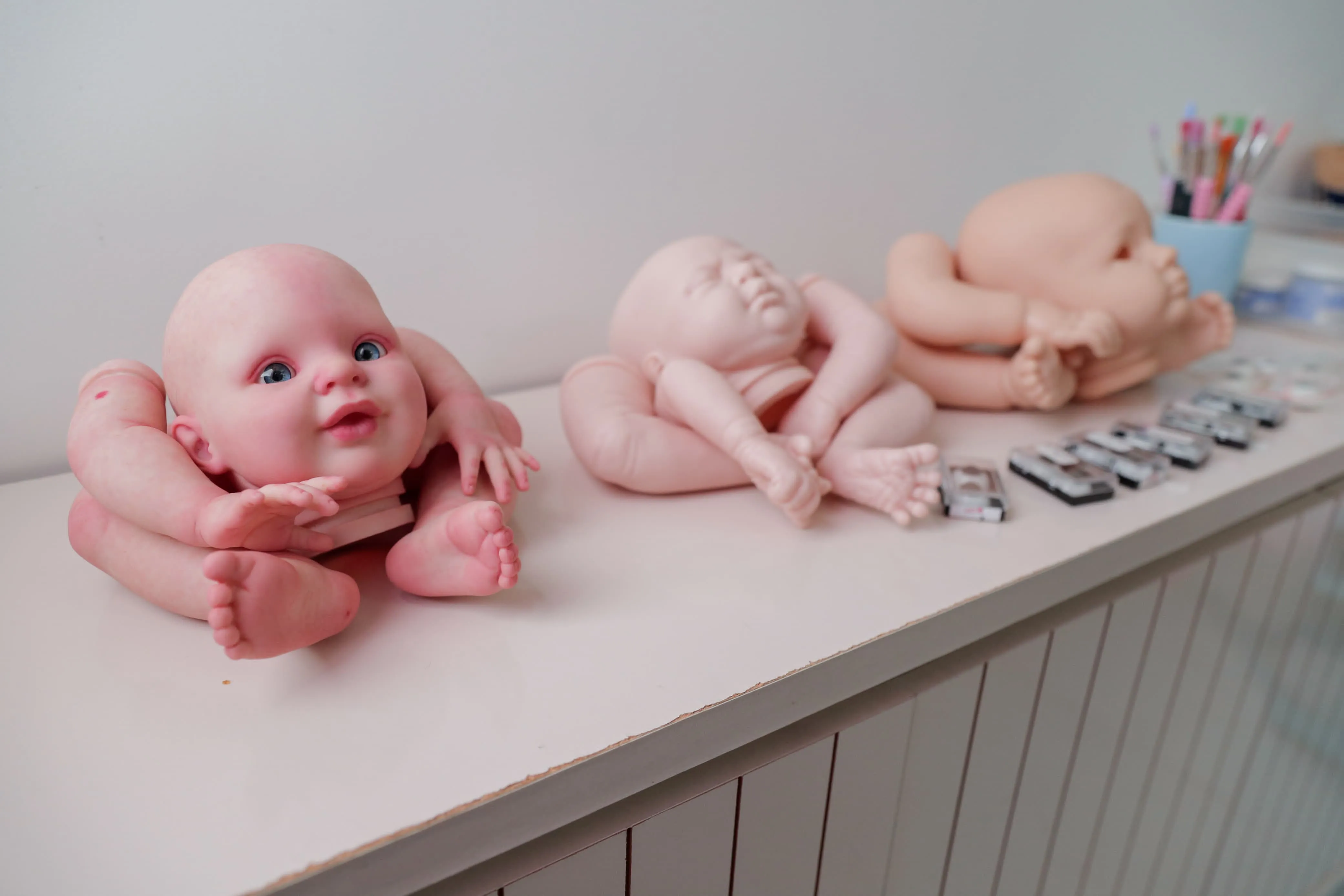 À esquerda, um bebê com o processo de pintura já iniciado. Os dois na sequência ainda estão na forma original.
