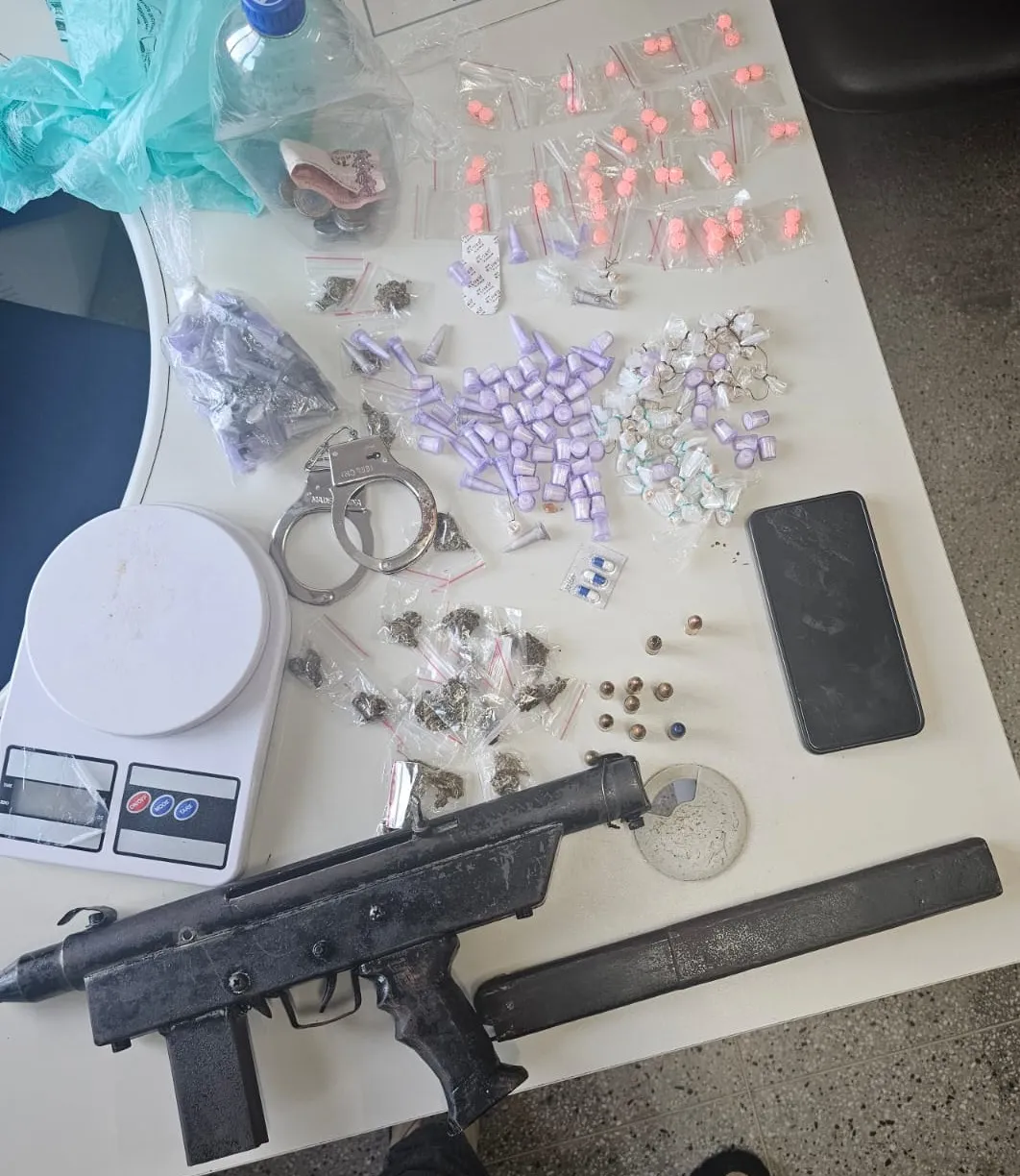 No interior da mochila que o suspeito carregava, foram encontrados uma submetralhadora artesanal 9mm, munições, 68 porções de cocaína, 46 de droga sintética e 55 pedras de crack, além de um par de algemas e uma balança de precisão